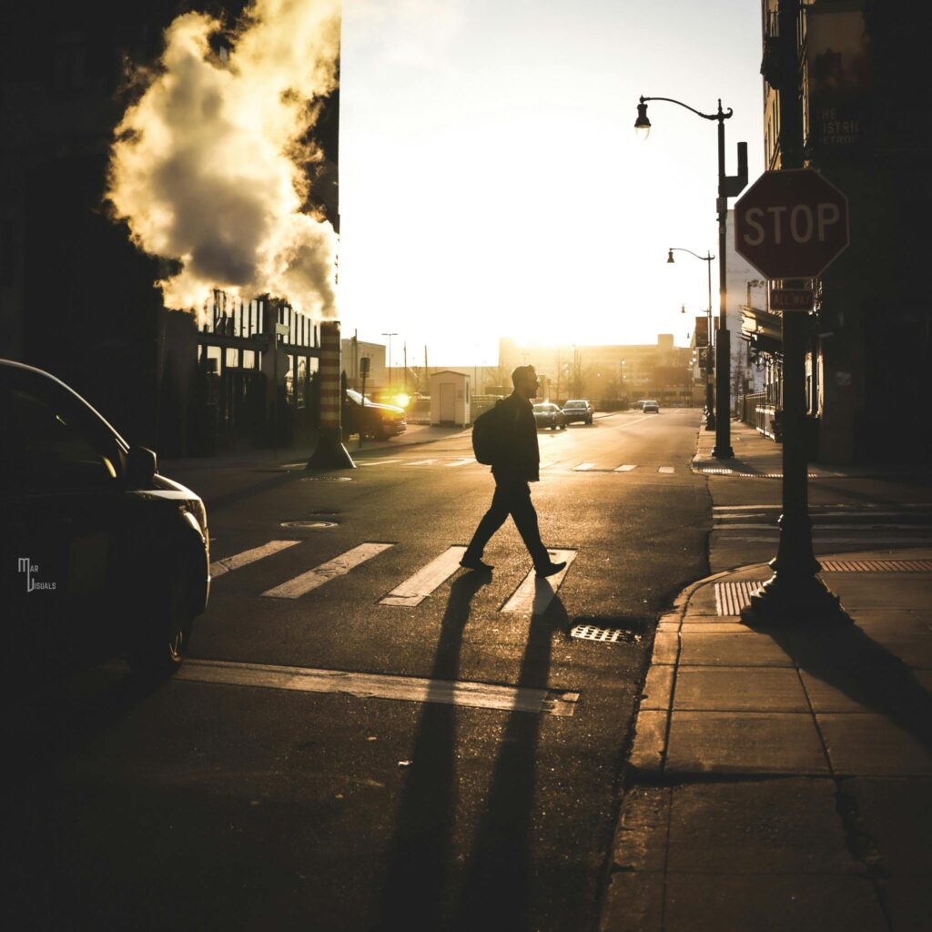 A silhouette of a man walking across a street in an urban setting at sunrise, highlighting city life.