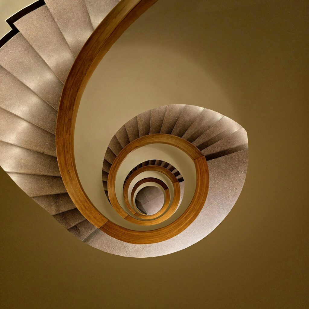 Elegant spiral staircase with wooden handrails viewed from above in a modern building setting.