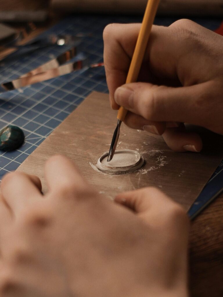 A detailed view of hands working on a jewelry mold using a tool, showcasing craftsmanship.