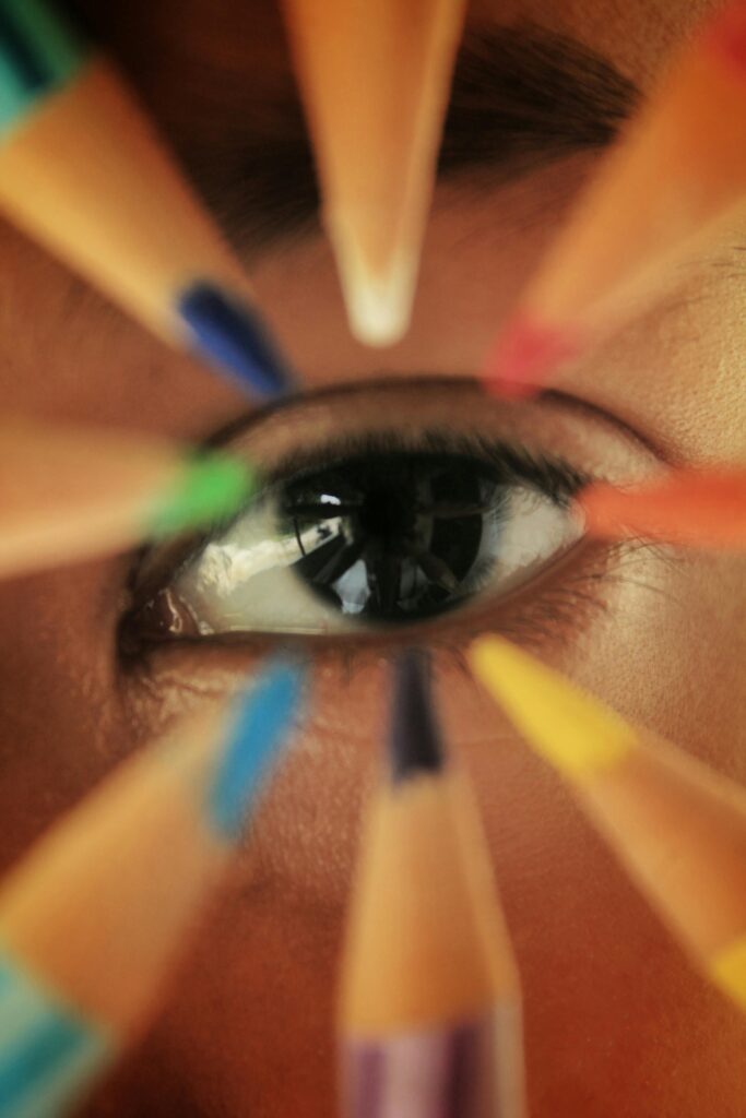 Close-up of a human eye surrounded by a vibrant array of colored pencils in macro photography.